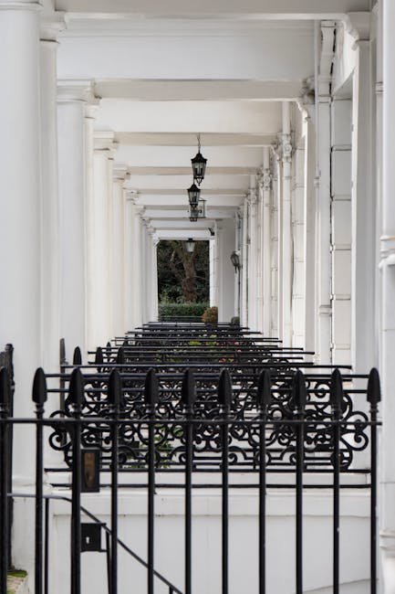 An outdoor scene along a paved walkway in South Kensington featuring white residential buildings with classical architectural details. A black wrought iron fence runs parallel to the sidewalk, with so