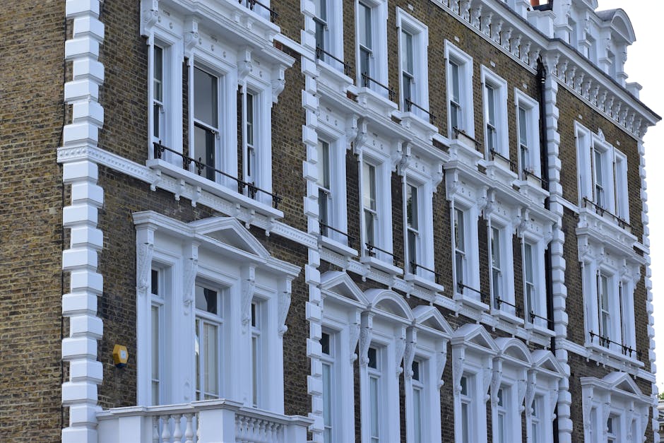 A row of Victorian-style terraced houses with multi-colored facades, including shades of blue, beige, and green, situated along a street in South Kensington. The buildings feature tall, arched windows with white frames, some with decorative molding, and are topped with intricate cornices. A black lamppost is visible in the foreground, and the street appears clean and well-maintained. The natural daylight illuminates the facades, highlighting their architectural details. This scene reflects the elegant residential character typical of South Kensington, where professional cleaning services by Cleaners South Kensington ensure the upkeep and hygiene of such properties, especially useful for end of tenancy cleaning and maintaining domestic cleanliness.