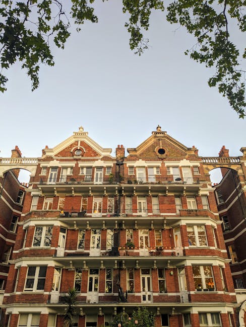 The image depicts the facade of a historic multi-story residential building constructed with red brick and cream-colored stone detailing, characteristic of Victorian architecture. The building feature